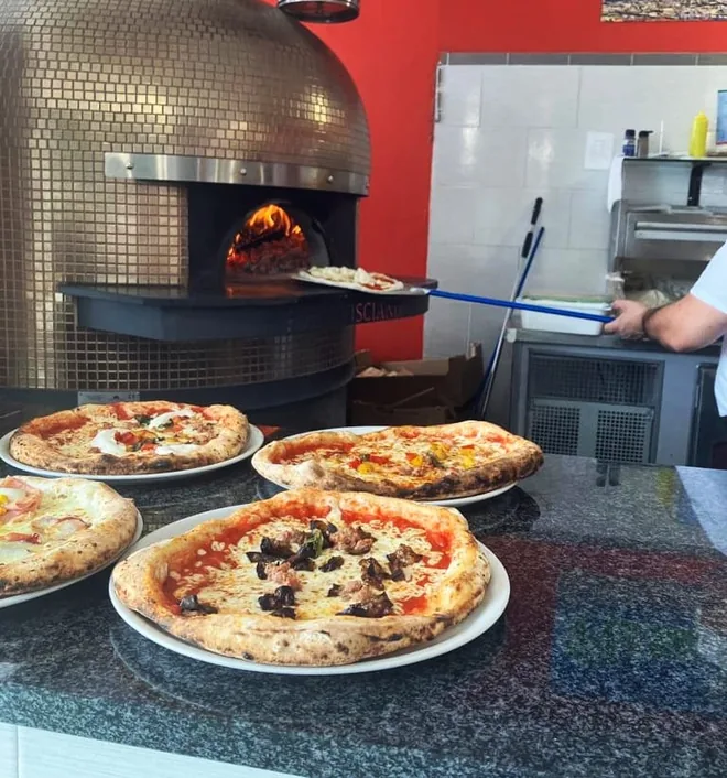 Il forno acceso e tre pizze appena sfornate sul banco